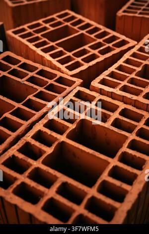 High-angle close-up of stacked terracotta clay hollow brick blocks, showing their geometric internal honeycomb structures. Selective focus. Stock Photo