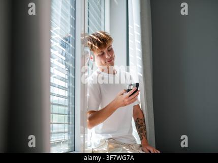 .Young man browsing smartphone during quiet afternoon at home. Stock Photo