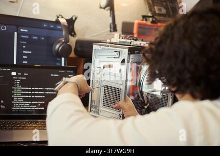 young Asian male technician repairing computer hardware using screwdriver. Image represents IT support, system maintenance, and technology education, over shoulder shot Stock Photo