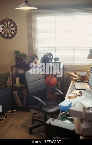Vertical image of empty home office workspace featuring laptop on desk and black leather chair, representing remote work lifestyle and freelance career marketing Stock Photo