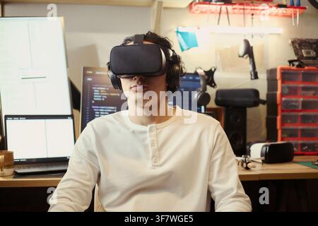 Young Asian man wearing virtual reality headset in home office workspace. Image represents immersive technology development and is suitable for IT training marketing Stock Photo