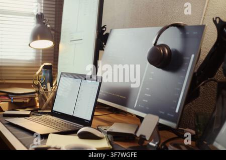 Computer monitors and laptop displaying software code on wooden desk in home office, representing remote work and programming. Ideal for IT training and software development marketing Stock Photo