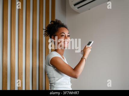 Young woman setting home temperature using air conditioner remote. Stock Photo