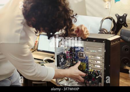 Young Asian man repairing desktop computer motherboard at desk, representing IT support and hardware maintenance. Image suitable for technology services advertising Stock Photo