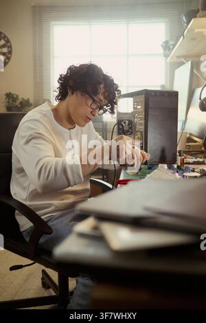 Young Asian man soldering computer motherboard at desk, repairing hardware components. Image suitable for IT support services, tech education, and engineering career promotions, vertical Stock Photo