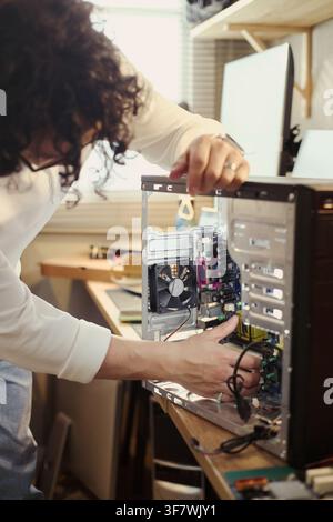 Vertical image of Young Asian man repairing desktop computer hardware at workshop desk, representing IT support and tech maintenance services for commercial marketing Stock Photo