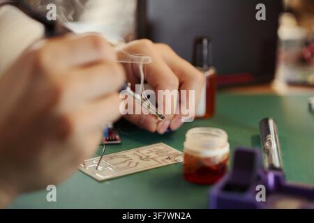 Hands of Young Asian man soldering electronic components on circuit board. Image represents engineering education and hardware development, suitable for tech training promo Stock Photo
