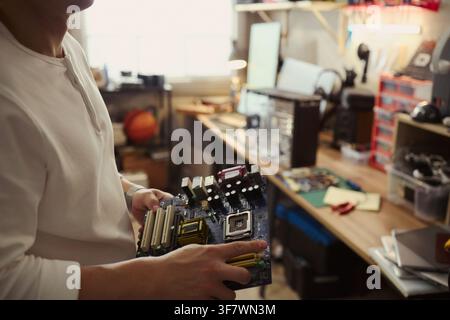 Cropped shot of Young Asian man holding computer motherboard in workshop, repairing hardware. Image represents IT support and tech services, suitable for computer repair ads Stock Photo