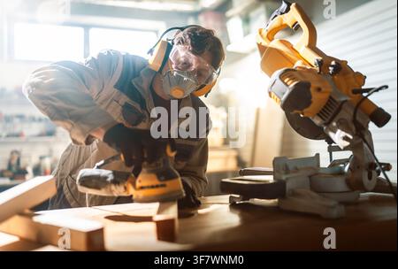 Focused craftsman working in a sunlit workshop, sanding a wooden plank with precision using professional power tools. The individual is equipped with Stock Photo