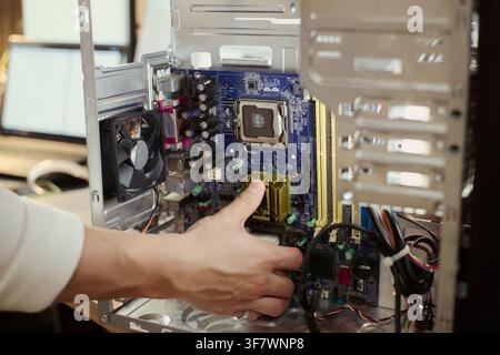 Asian male technician hand installing hardware component inside open computer tower, upgrading system motherboard. Image suitable for IT support and hardware repair services Stock Photo