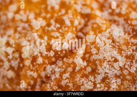 Extreme close-up of a golden baked pastry surface covered with coarse sugar crystals, creating a warm appetizing food texture and abstract bakery back Stock Photo