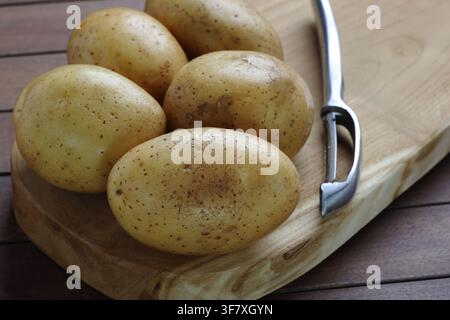 Fresh Raw Yellow Potatoes on Wooden Cutting Board with Vegetable Peeler Stock Photo