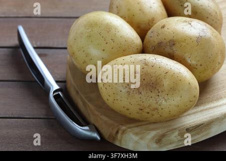 Fresh Raw Yellow Potatoes on Wooden Cutting Board with Vegetable Peeler Stock Photo