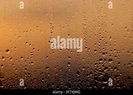 Orange-tinted glass with water droplets, moisture on the window in the form of condensation drips and small drops of water in the evening light Stock Photo