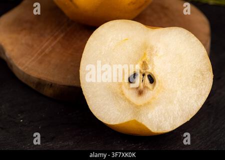 A yellow pear with white flesh on the slice, the slices of the pear product lie on a wooden cutting surface against a background of dark black slate. Stock Photo