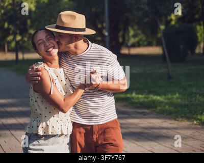 A young couple shares a playful and affectionate moment while walking together in park. Stock Photo