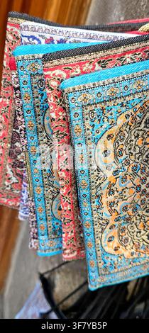 A close view of layered woven textiles with intricate floral and geometric patterns in blue, red, beige and black, displayed among decorations associa Stock Photo