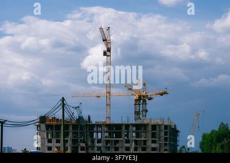 New apartment building under construction featuring several tall tower cranes, highlighting ongoing real estate development and urban expansion in a bustling city environment Stock Photo