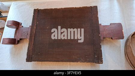 A traditional wooden mold for making waffles or prosphora sits on a white linen surface. The mold shows a detailed grid pattern, highlighting its anti Stock Photo