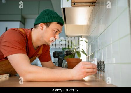 Skilled handyman installing multiple wall sockets on tiled backsplash in a contemporary kitchen, performing electrical work and household repairs during renovation Stock Photo