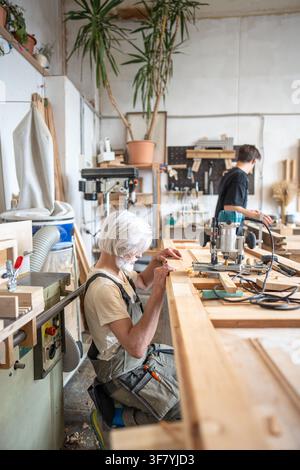 Focused man restorer attentively checking wooden door surface at workplace in restoration workshop. Stock Photo