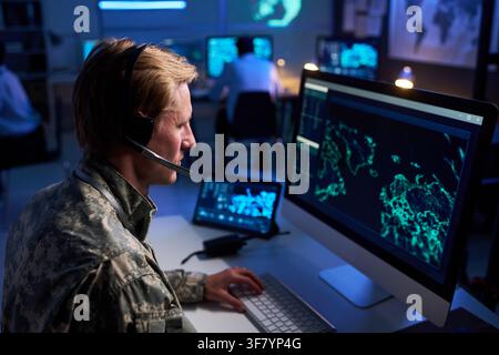 Military Officer Wearing Headset Working on Cybersecurity in Control Room Stock Photo