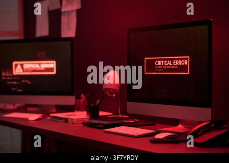 Computer Screens Showing Critical Error Message in Dark Office Stock Photo
