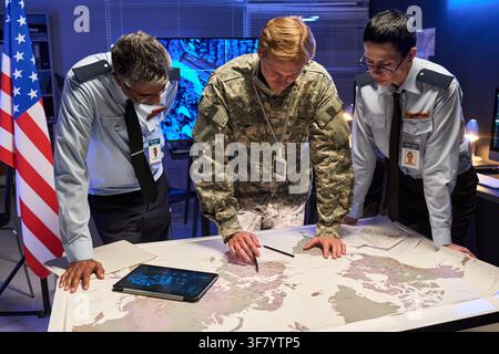 Military Officers and Soldier Analyzing World Map in Command Center Stock Photo