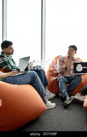 A group of young professionals collaborates on an artificial intelligence project, using laptops and discussing ideas in a modern office setting with Stock Photo