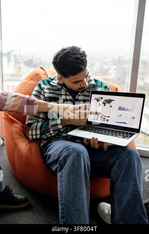 Two colleagues collaborate on a laptop displaying world map and financial charts, discussing business strategy and growth Stock Photo