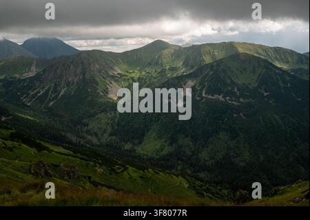 Sun breaking through storm clouds over green mountains Stock Photo