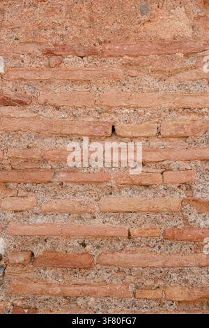 Detail of an old wall made of irregular, worn, reddish-brown, elongated bricks joined horizontally with gray cement. Front view. Stock Photo