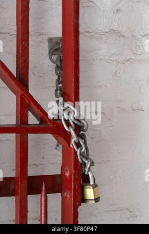 LONDON, UK - JULY 14, 20026:  Brass padlock and chain on open red metal  gate Stock Photo
