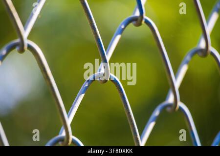 Close-up shot of a galvanized metal chain-link fence with a soft green background and an amazing backlit Stock Photo