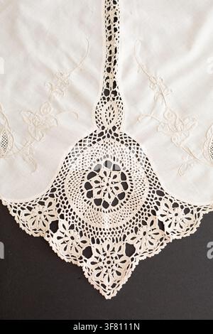 Detail of a crocheted and cross-stitched tablecloth on a black background, border decoration. Crafts, vintage linens. Hobby concept. Top view. Natural Stock Photo