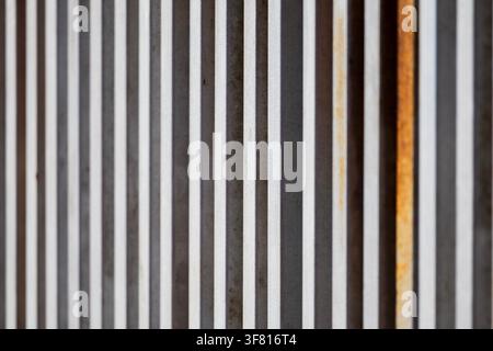 Close-up of a contemporary gate with vertical metal slats in varying shades of gray and rust Stock Photo