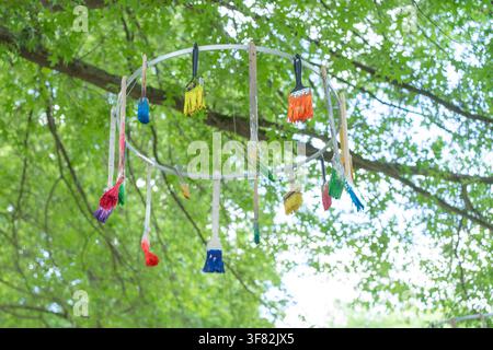 A charming outdoor display of paintbrushes with wooden handles and synthetic bristles, hanging under a tree in a playful and creative manner Stock Photo