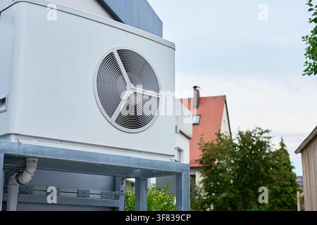 Outdoor heat pump unit installed next to a residential building. Close-up of modern home heating and cooling equipment with a large fan mounted on a m Stock Photo