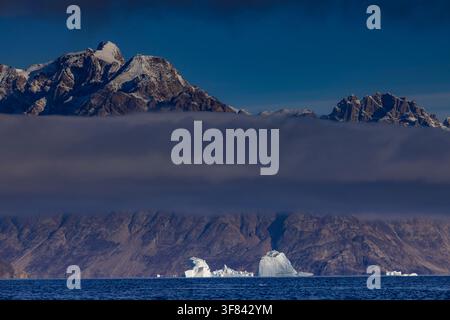 Icebergs float in the ocean beneath a striking cloud band over Warming Island in Greenland Stock Photo