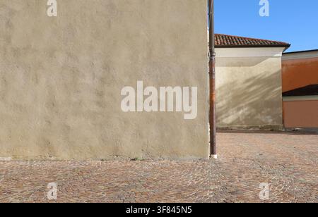 Rusty gutter at the corner of a cream colored plaster old wall. A orange wall, roof and sky on background. Porphyry pavement in front Background Stock Photo