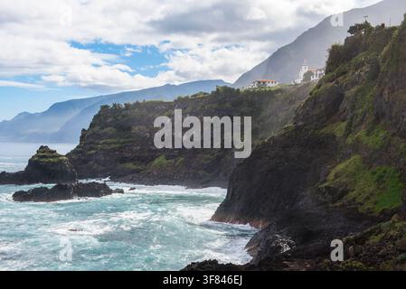 Coastline with rocky cliffs and ocean waves near Seixal in Madeira, Portugal on a clear day with clouds in the sky Stock Photo