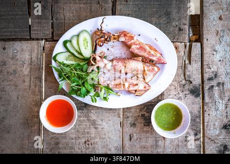 Grilled squid served with herbs and sauces on a wooden table in Vietnam for a traditional dining experience Stock Photo