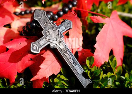 Black ebony rosary with carved crucifix placed on vibrant red autumn leaves for seasonal reflection in France Stock Photo