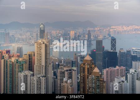 View of Hong Kong skyline from Victoria Peak at sunset with city lights appearing over Kowloon Peninsula and surrounding mountains Stock Photo