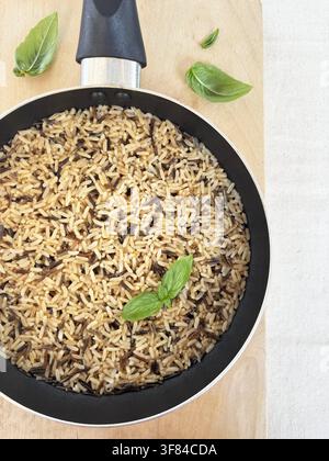 A mix of brown and wild rice cooked in a pan with fresh basil, perfect to express the concept of wellness, healthy eating and natural homemade cuisine. Stock Photo