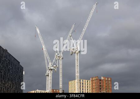 Construction cranes against cloudy sky in urban development Stock Photo