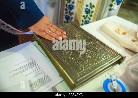 A man places his hand on an ornate metal gospel book during a church wedding ceremony. Stock Photo