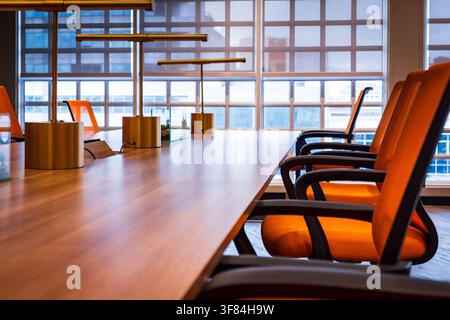 Modern conference room with wooden table, orange chairs, and brass table lamps, empty boardroom interior. Stock Photo