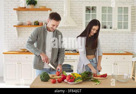 Happy young family couple, man, woman cutting salad, helping, healthy vegans cooking at home Stock Photo