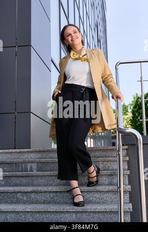 A young woman in cozy clothes walks happily down sunlit stone steps. Stock Photo